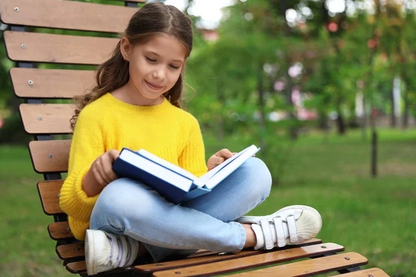 Linda niña leyendo libro sobre tumbona en el parque — Foto de Stock