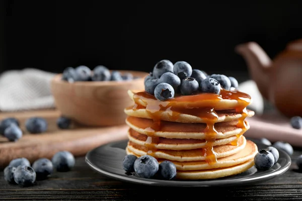 Pancake lezat dengan blueberry segar dan sirup karamel di atas meja kayu hitam — Stok Foto