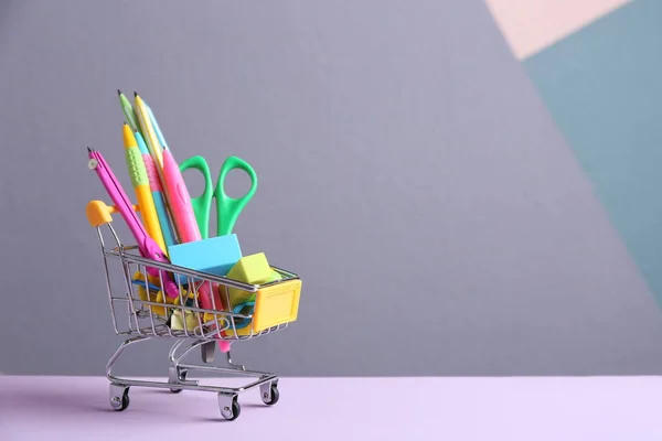 Small shopping cart with different school stationery on color background. Space for text — Stock Photo, Image