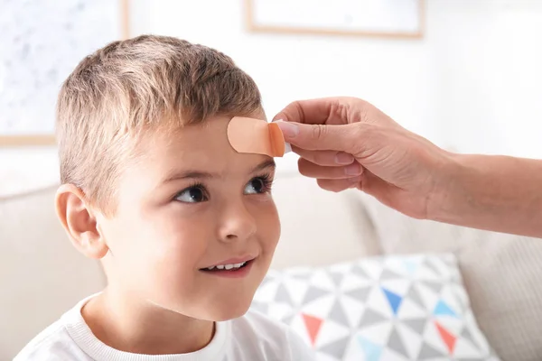 Woman applying adhesive bandage on boy's forehead indoors — Stock Photo, Image