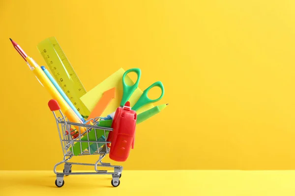 Pequeno carrinho de compras com diferentes artigos de papelaria escolar em fundo amarelo. Espaço para texto — Fotografia de Stock