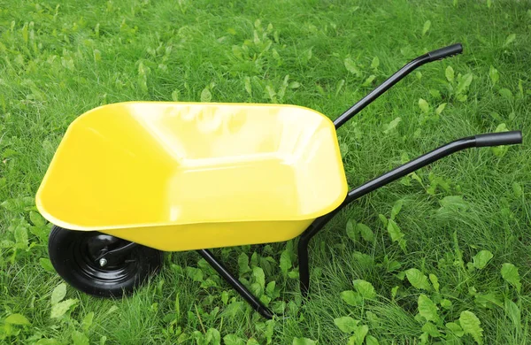 Yellow wheelbarrow on green grass outdoors. Gardening tool — Stock Photo, Image
