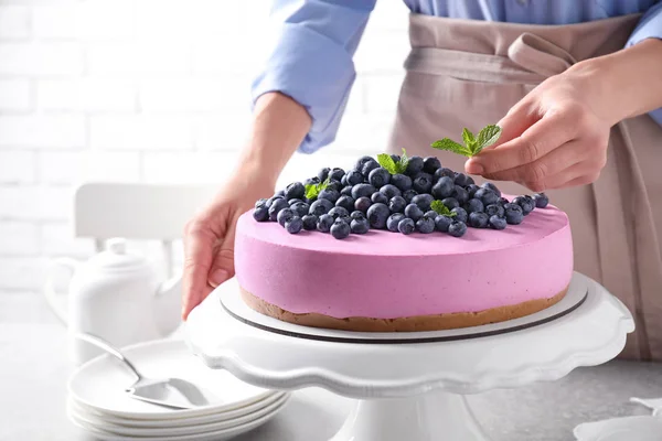 Jovem mulher decorando saboroso bolo de mirtilo com hortelã à mesa, close-up — Fotografia de Stock