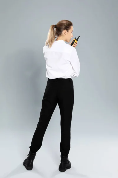 Female security guard in uniform using portable radio transmitter on grey background
