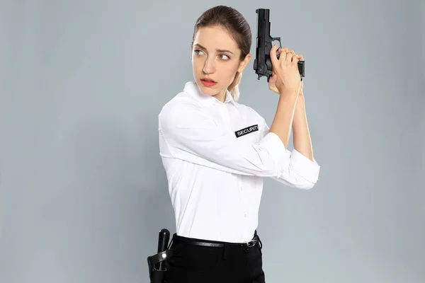 Female security guard in uniform with gun on grey background