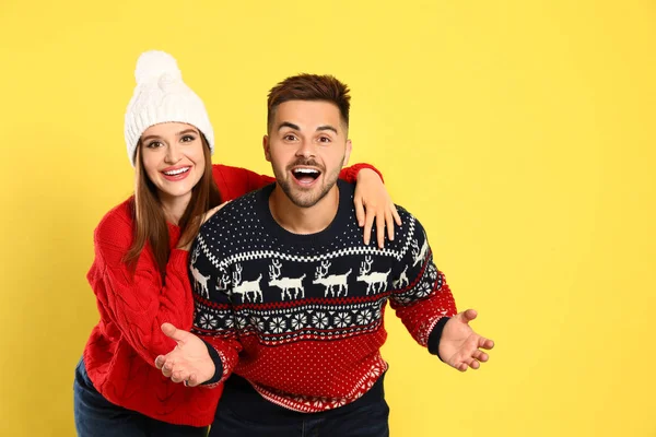 Pareja vistiendo suéteres de Navidad sobre fondo amarillo — Foto de Stock