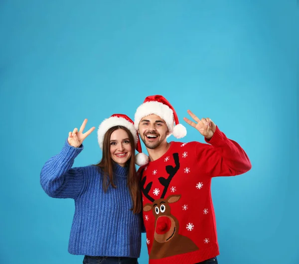 Casal usando camisolas de Natal e chapéus de Papai Noel no fundo azul — Fotografia de Stock