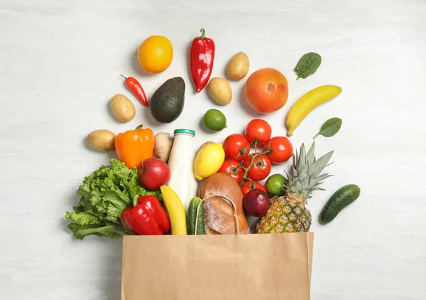 Shopping paper bag with different groceries on white wooden background, flat lay — Stock Photo, Image