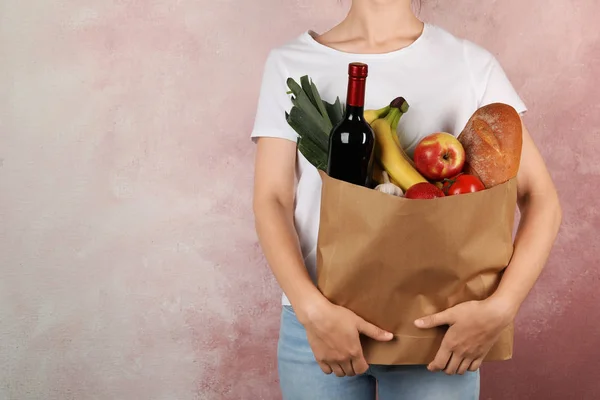 Frau hält Einkaufstasche mit verschiedenen Lebensmitteln vor rosa Hintergrund. Raum für Text — Stockfoto