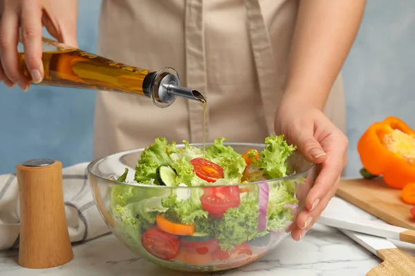 Woman dressing tasty fresh Greek salad with olive oil at white marble table, closeup