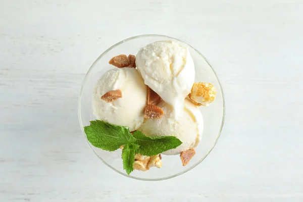 Вкусное мороженое с карамельными конфетами и попкорном в миске для десерта на белом деревянном столе, вид сверху — стоковое фото