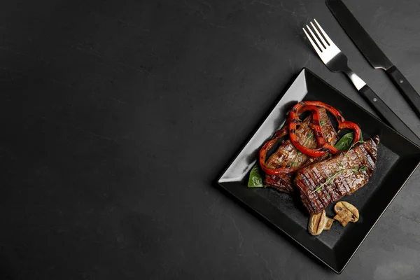 Gegrild vlees geserveerd met garnituur op zwarte tafel, platte lag. Ruimte voor tekst — Stockfoto