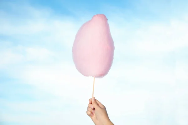 Woman holding sweet pink cotton candy on blue sky background, closeup view — Stock Photo, Image