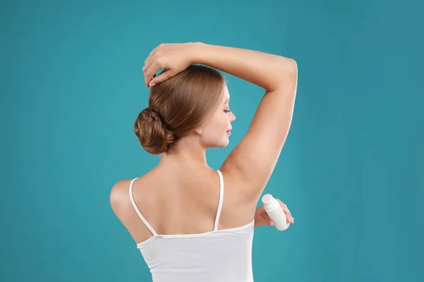 Young woman applying deodorant to armpit on teal background — Stock Photo, Image