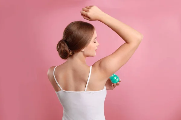 Jovem aplicando desodorizante para axila no fundo rosa — Fotografia de Stock
