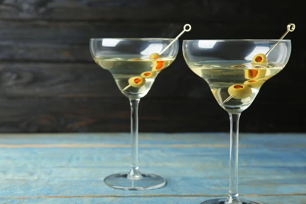 Klassiska Dry Martini-glas med Oliver på ljusblå träbord mot mörk bakgrund — Stockfoto