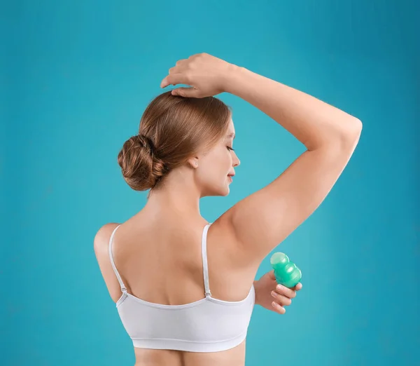 Mujer joven aplicando desodorante a la axila sobre fondo verde azulado — Foto de Stock