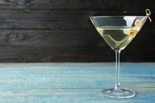 Glas klassischer trockener Martini mit Oliven auf hellblauem Holztisch vor dunklem Hintergrund. Raum für Text — Stockfoto