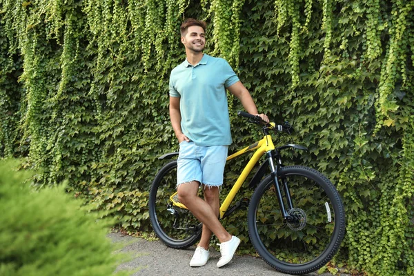 Красивий молодий чоловік з велосипедом біля стіни вкритий зеленими ліанами плюща на міській вулиці — стокове фото