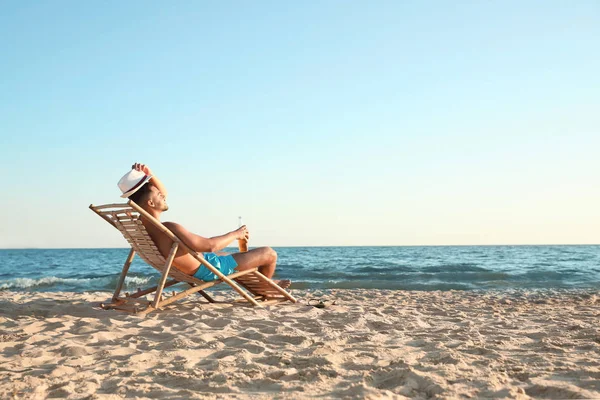 Jonge man ontspannen in ligstoel op het strand in de buurt van zee — Stockfoto