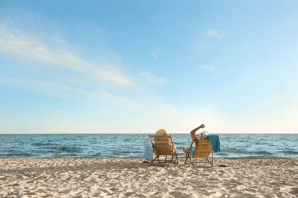 stock image Young couple relaxing in deck chairs on beach near sea