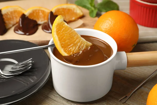 Orangenscheibe in Fonduetopf mit Vollmilchschokolade auf Holztisch tauchen, Nahaufnahme — Stockfoto