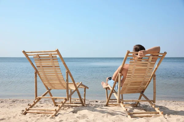 모래 해변에서 갑판 의자에서 휴식을 취하는 젊은 남자 — 스톡 사진