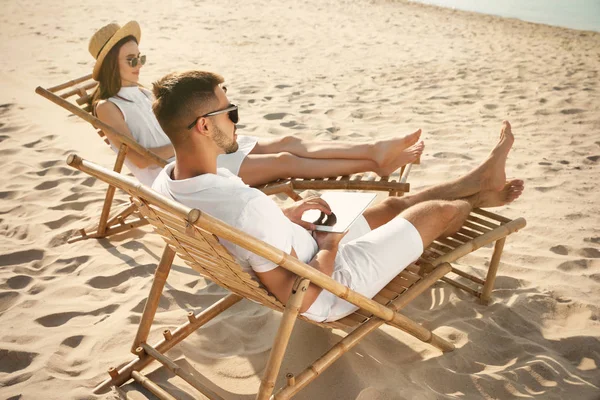 Jovem casal relaxante em espreguiçadeiras na praia de areia — Fotografia de Stock