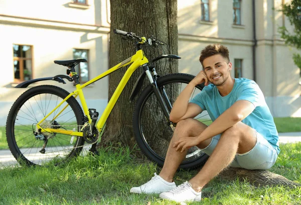 Красивий молодий чоловік сидить біля велосипеда на зеленій траві — стокове фото