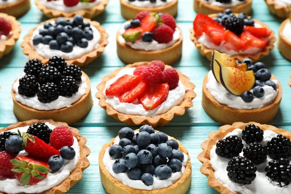 Many different berry tarts on blue wooden table. Delicious pastries — Stock Photo, Image