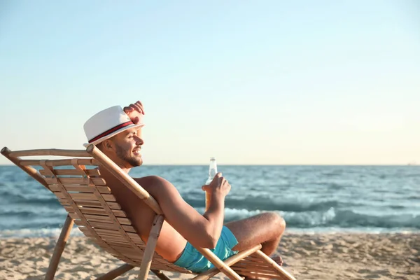 Giovane uomo rilassante sulla sedia a sdraio sulla spiaggia vicino al mare — Foto Stock