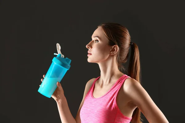 Athletische junge Frau trinkt Proteinshake auf schwarzem Hintergrund — Stockfoto