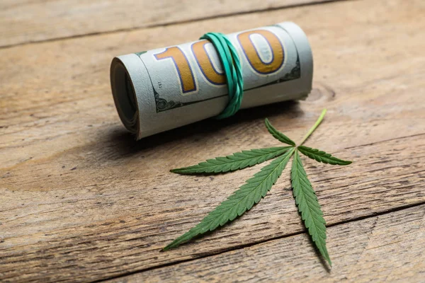 Hemp leaf and rolled money on wooden background, closeup