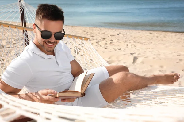 Молодой человек читает книгу в гамаке на пляже — стоковое фото