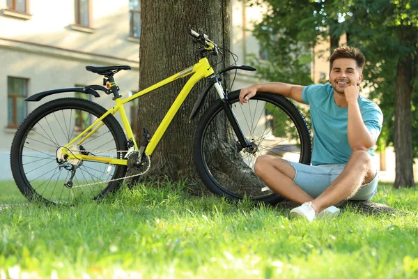 Красивий молодий чоловік сидить біля велосипеда на зеленій траві — стокове фото