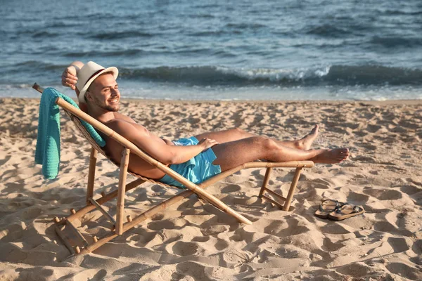 Hombre joven relajándose en la silla de cubierta en la playa cerca del mar — Foto de Stock