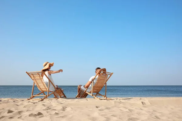 Pareja joven relajándose en tumbonas en la playa — Foto de Stock