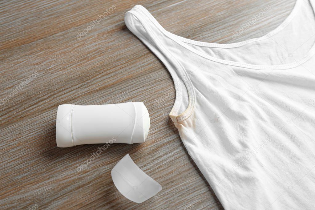 White undershirt with stain and deodorant on wooden background