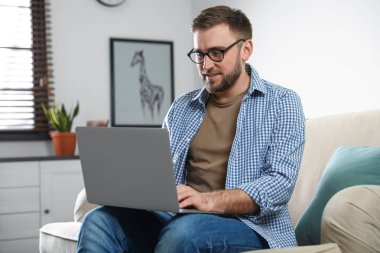 Genç adam oturma odasında dizüstü bilgisayar kullanıyor.