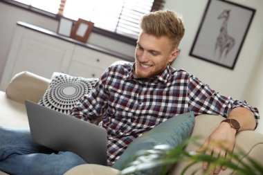 Genç adam oturma odasında dizüstü bilgisayar kullanıyor.