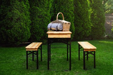 Parkta ahşap masa üzerinde battaniye ile Hasır piknik sepeti