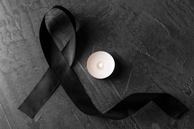 Black ribbon and burning candle on dark grey stone surface, top view. Funeral symbols clipart