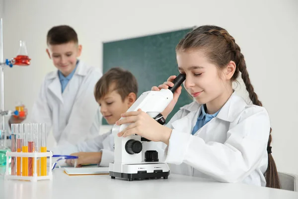 Menina inteligente olhando através do microscópio e seus colegas na aula de química — Fotografia de Stock