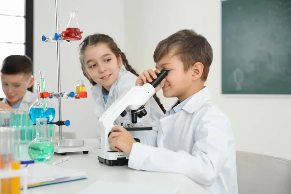 Colegial mirando a través del microscopio y sus compañeros en la lección de química — Foto de Stock