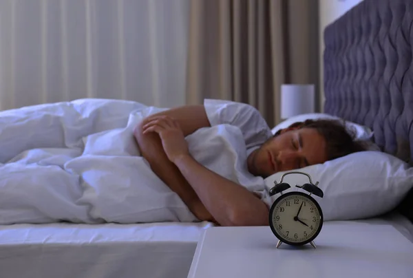 Väckarklocka på nattduksbord nära sovande ung man. Sänggåendet — Stockfoto