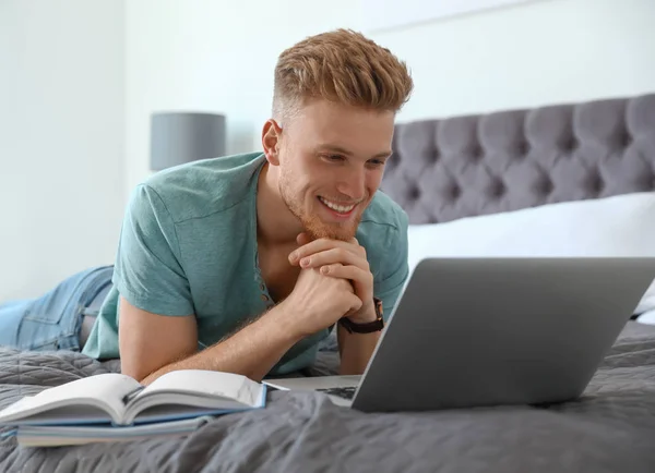 Junger Mann benutzt Laptop, während er zu Hause im Bett liegt — Stockfoto