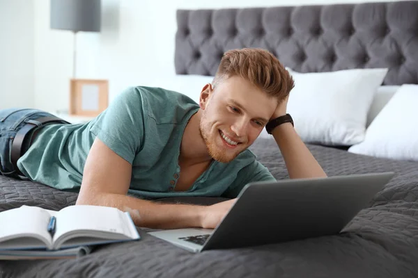 Junger Mann benutzt Laptop, während er zu Hause im Bett liegt — Stockfoto