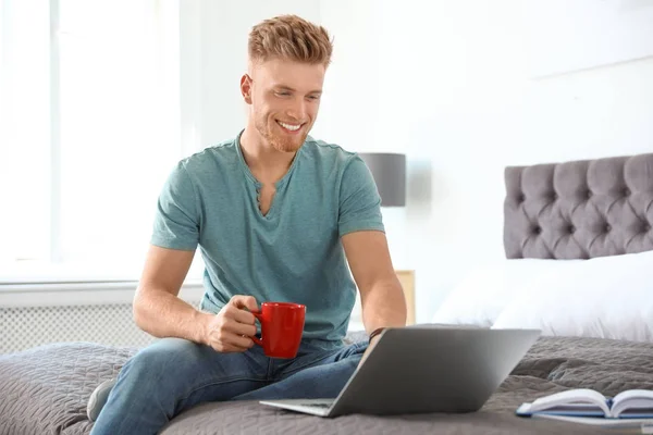 Junger Mann benutzt Laptop, während er zu Hause auf dem Bett sitzt — Stockfoto