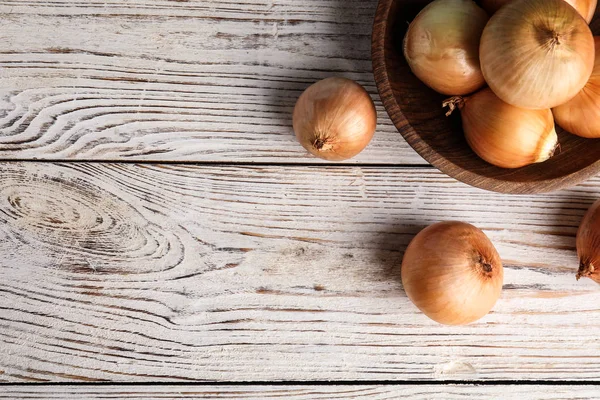 Bowl en rijpe uien op witte houten tafel, platte lag. Ruimte voor tekst — Stockfoto