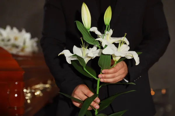Молодой человек с белыми лилиями в похоронном бюро, крупный план — стоковое фото